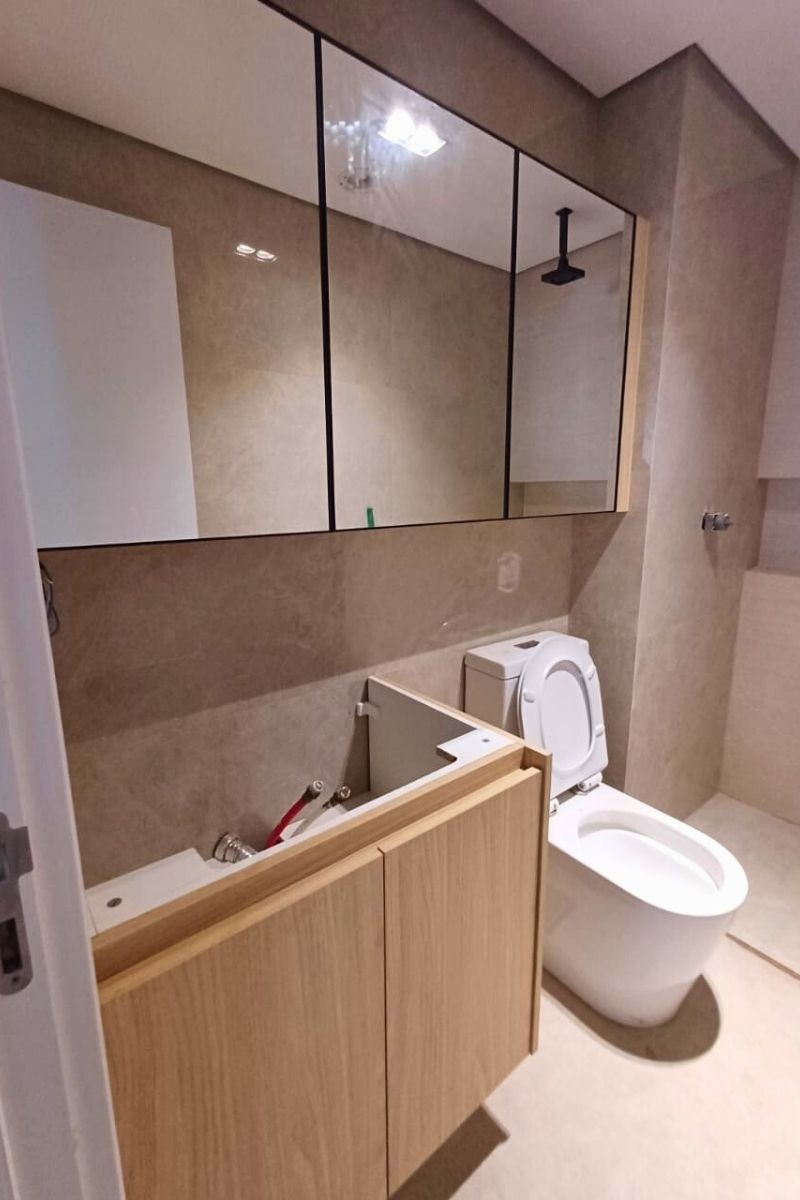 Banheiro em fase de acabamento com gabinete planejado em madeira clara, combinando com o revestimento de porcelanato bege.