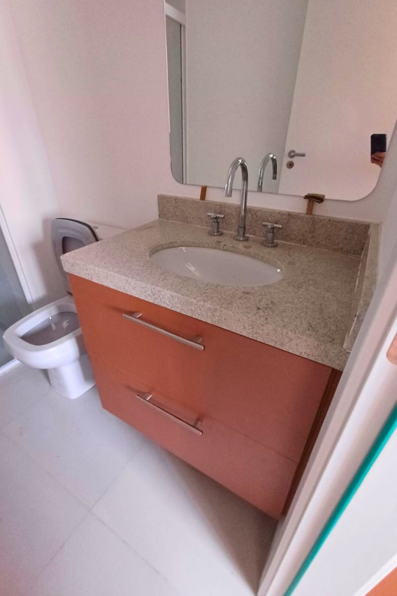 Gabinete de banheiro simples sob medida em tom amadeirado mogno, com tampo de granito e cuba de embutir oval.