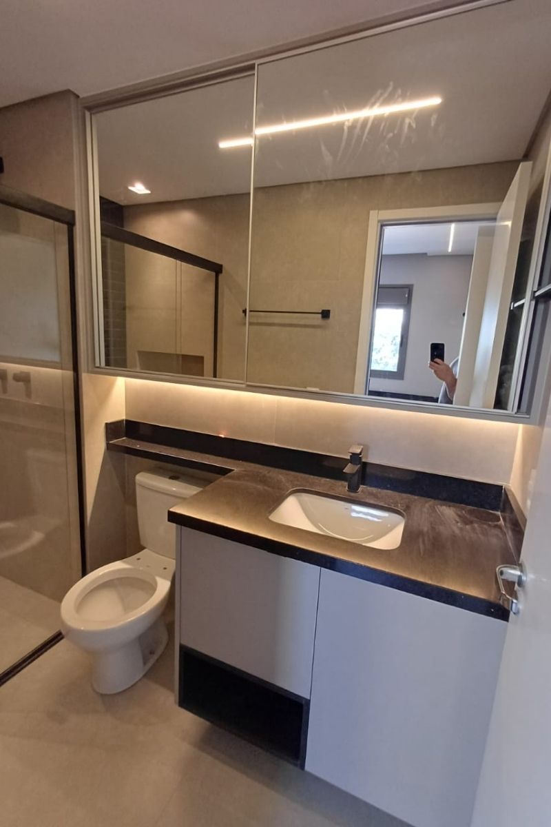 Banheiro moderno com bancada de granito preto absoluto, cuba de embutir e espelho amplo com fita de LED decorativa.