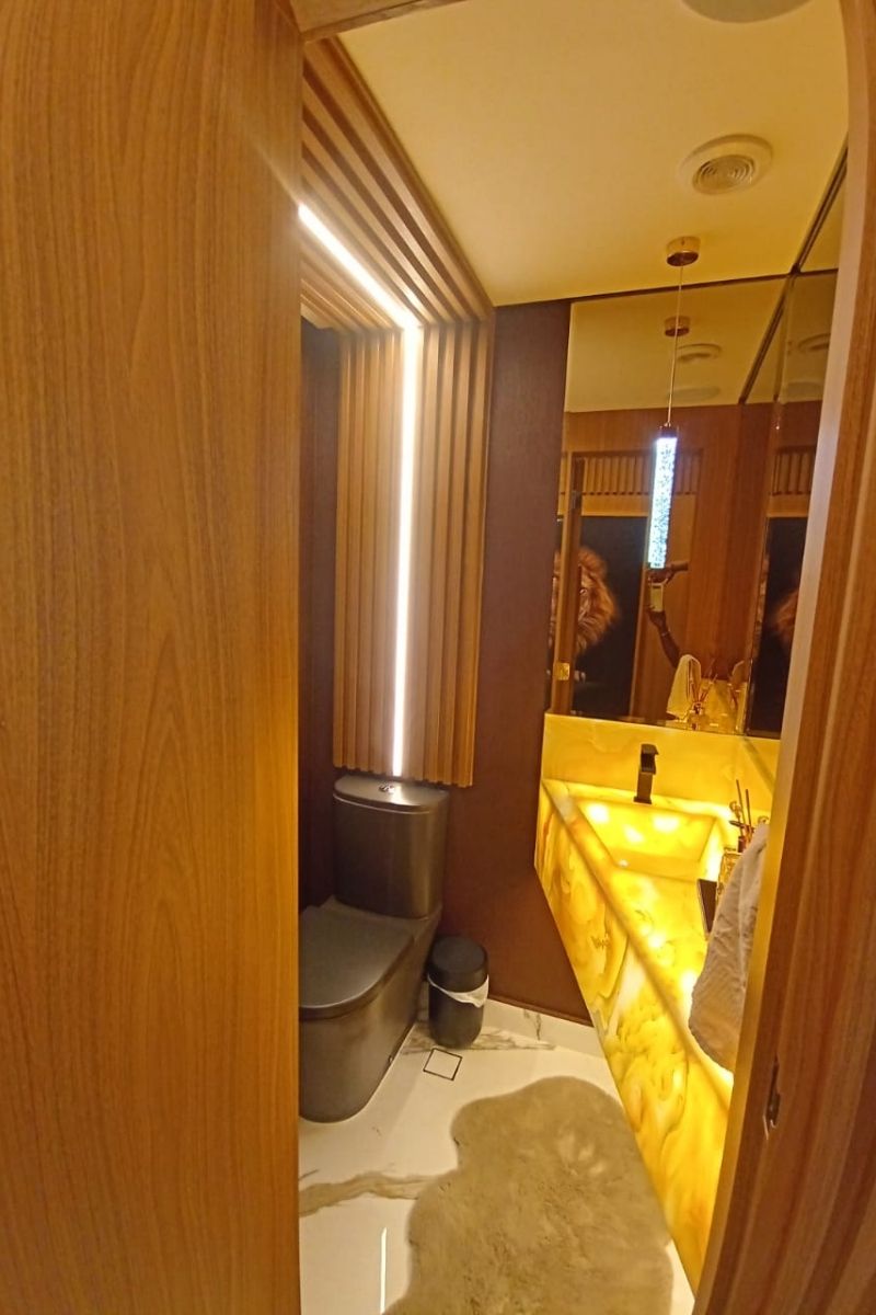 Lavabo de luxo com paredes revestidas em painel ripado de madeira e iluminação cênica vertical.