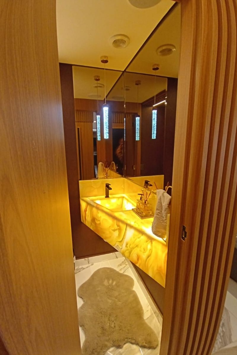 Destaque de projeto: bancada de lavabo em pedra onix translúcida iluminada (backlight) com torneira dourada sofisticada.