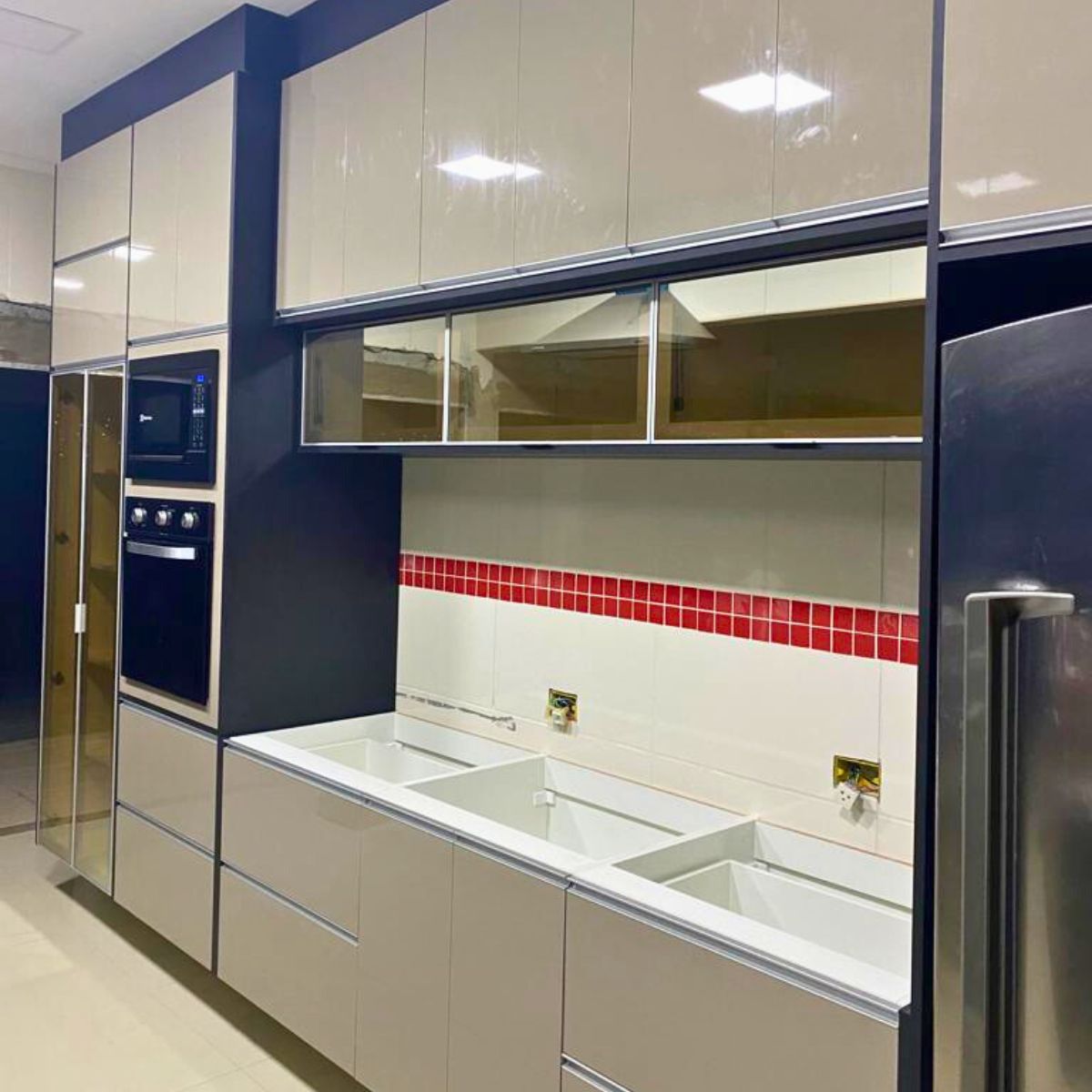 Projeto de cozinha moderna com armários em vidro reflexivo escuro (azul/preto) e detalhe em pastilhas vermelhas.