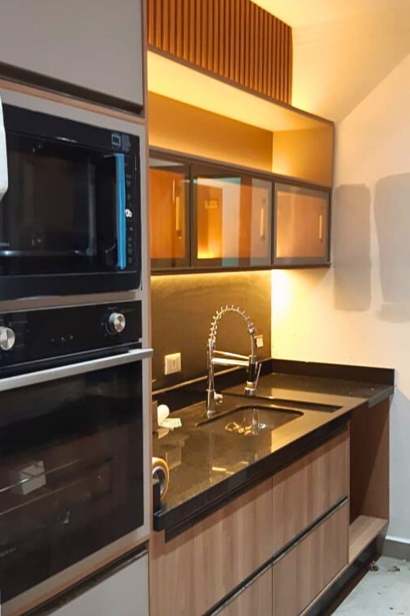 Torre quente planejada com fornos embutidos, iluminação LED na bancada e armários superiores com portas de vidro reflexivo bronze.