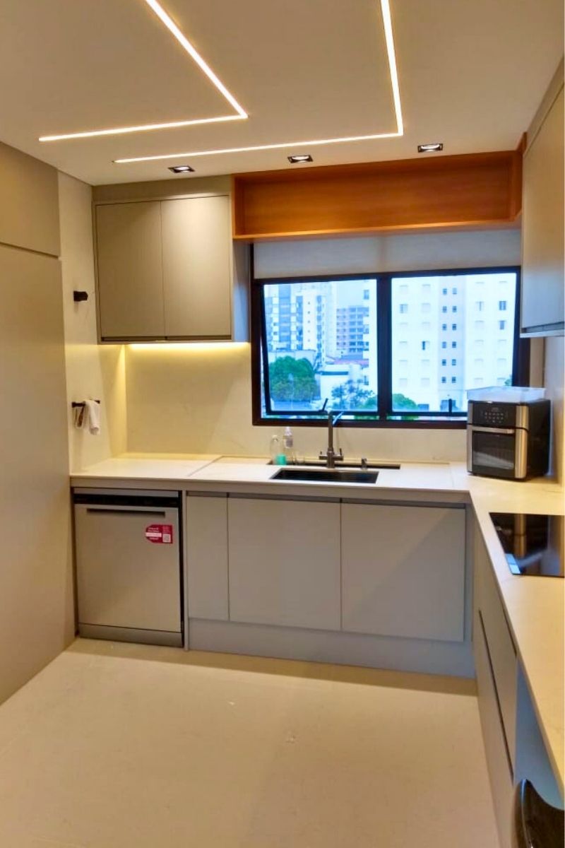 Bancada de cozinha planejada com iluminação LED embutida sob os armários superiores, destacando o revestimento e a pia.