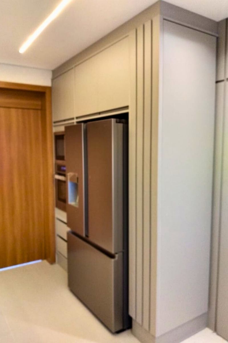 Detalhamento de marcenaria fina: painel ripado de madeira revestindo a lateral do nicho da geladeira e torre quente.