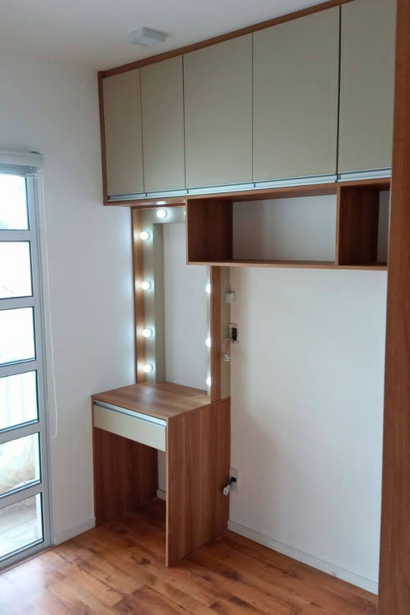 Penteadeira estilo camarim planejada, com espelho iluminado por lâmpadas e prateleiras em madeira, integrada ao quarto.