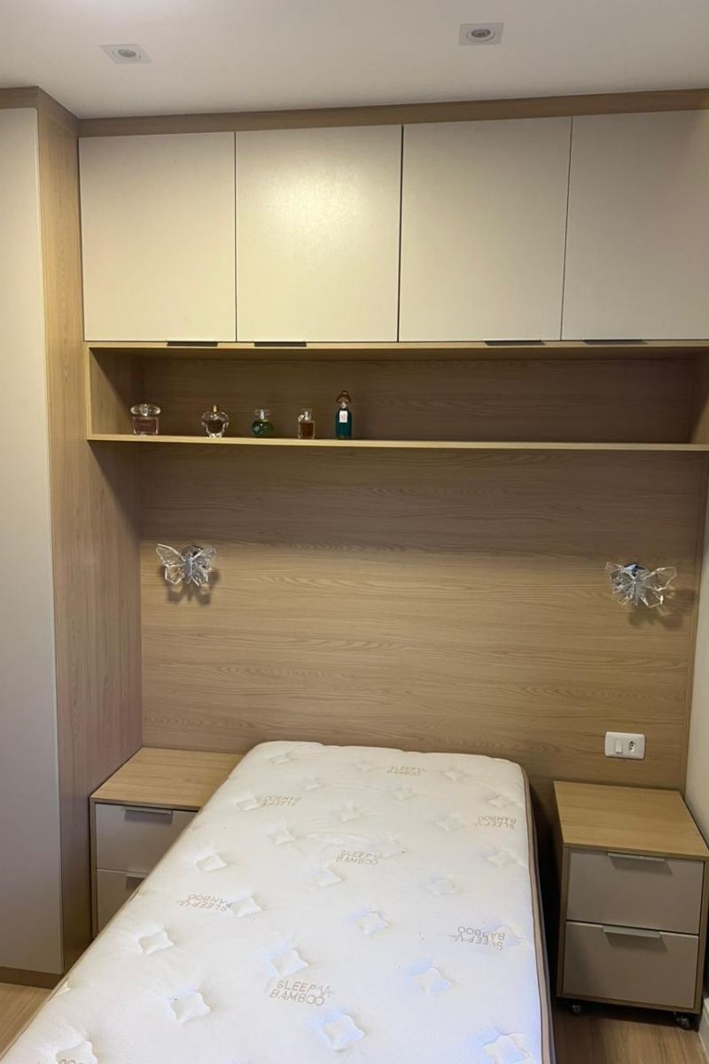 Painel de cabeceira planejado em madeira clara com prateleira superior para perfumes e decoração.