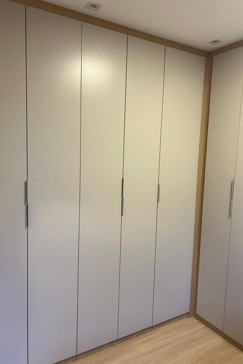 Guarda-roupa planejado branco com portas de batente e puxadores longos verticais, cobrindo toda a parede.