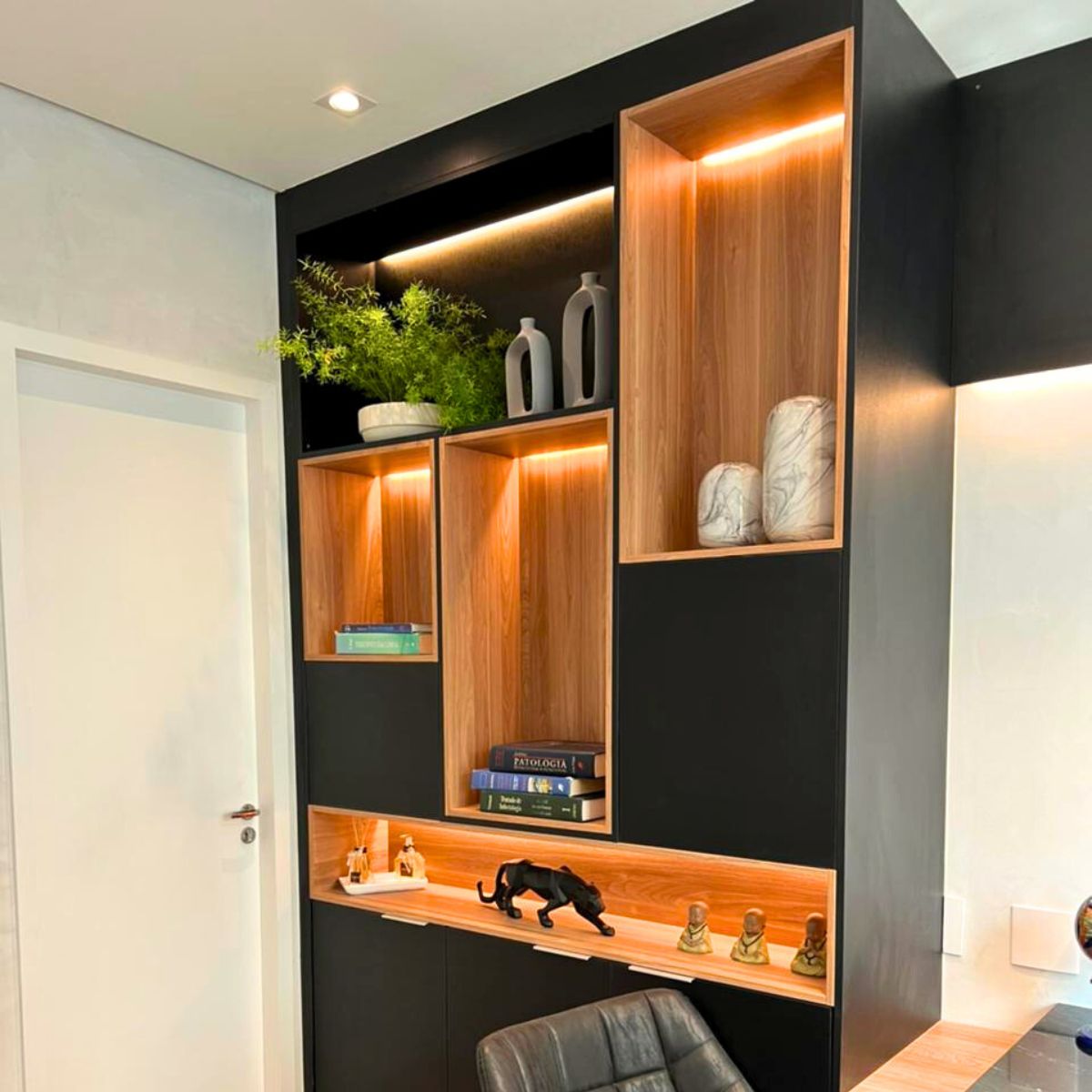 Estante decorativa planejada para home office em preto e madeira, com nichos iluminados por LED para livros e decoração.