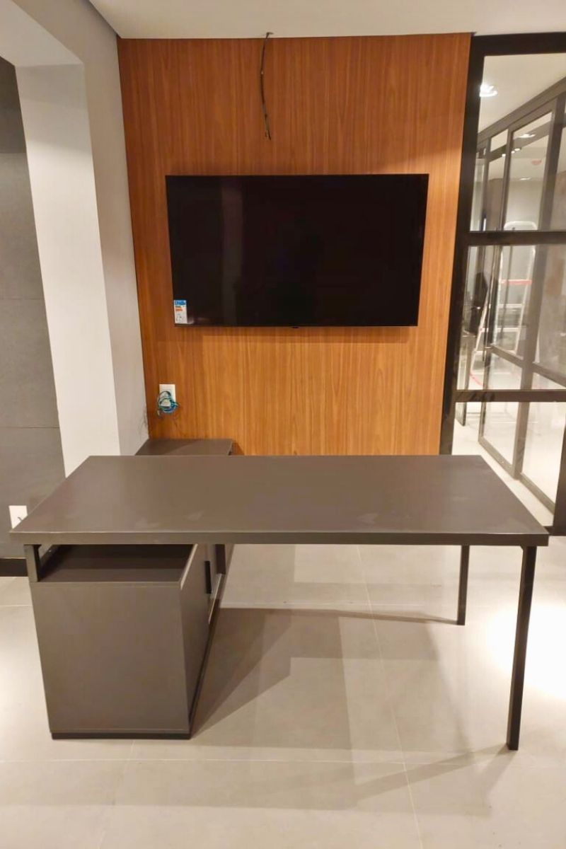 Estação de trabalho individual planejada com mesa escura e painel de TV em madeira ao fundo.
