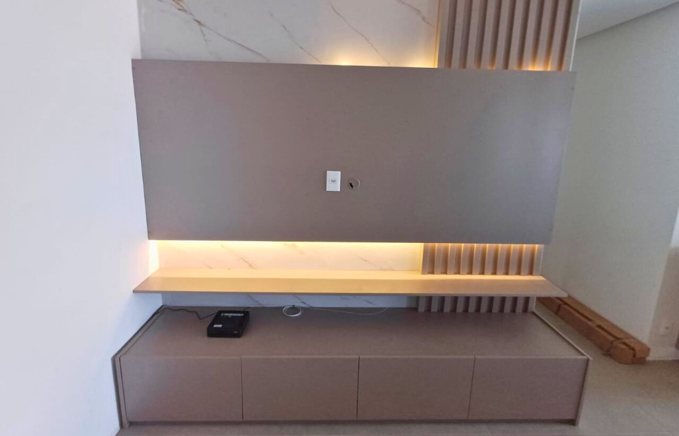 Móvel de sala planejado: painel suspenso cinza com prateleira iluminada por LED e rack com gavetas.