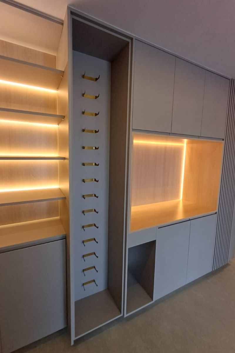 Detalhe de closet planejado de luxo com prateleiras de madeira iluminadas por fitas de LED e suportes organizadores dourados.